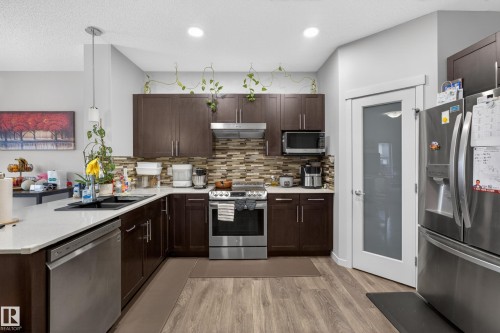 Kitchen featuring wood-finish flooring, stainless steel appliances, dark wood cabinetry, a mosaic tile backsplash, and white countertops - 1404 25 Avenue, Edmonton, AB 