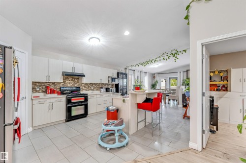 Kitchen featuring light-toned tile flooring, white cabinetry, a dark-toned range, and a breakfast bar island - 3519 22 Street Nw, Edmonton, AB 