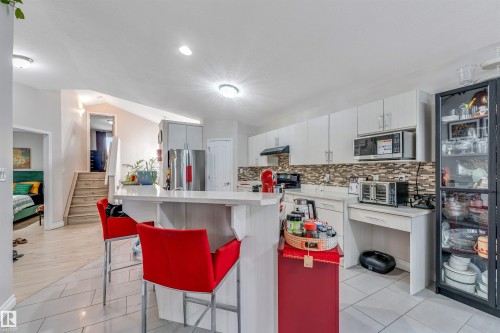 Contemporary kitchen featuring a breakfast bar with stone-finish countertop, white cabinetry, a tiled backsplash, and stainless steel appliances - 3519 22 Street Nw, Edmonton, AB 