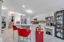 Contemporary kitchen featuring a breakfast bar with stone-finish countertop, white cabinetry, a tiled backsplash, and stainless steel appliances - 
