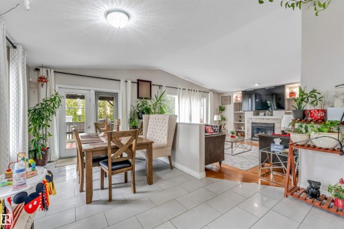 Open-concept living space featuring light tile flooring and hardwood flooring, with a fireplace and built-in shelving, French doors opening to an exterior area, and recessed lighting - 3519 22 Street Nw, Edmonton, AB 