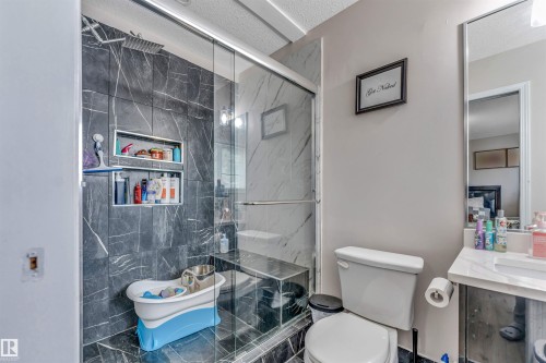 Glass-enclosed shower with dark marble-look tile, built-in shower niche shelving, and a rain shower head - 3519 22 Street Nw, Edmonton, AB 