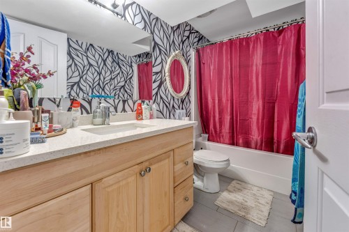 Bathroom featuring a wood-finish vanity with a light-colored countertop, an integrated sink, a rectangular mirror, and a wall-mounted light fixture - 3519 22 Street Nw, Edmonton, AB 