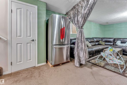 Carpeted interior space featuring a four-panel door, stainless steel refrigerator, and light green painted walls - 3519 22 Street Nw, Edmonton, AB 
