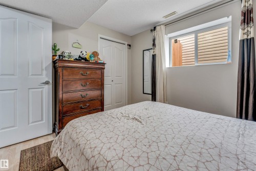 Bedroom featuring a window with blinds, wood-finish flooring, two panel doors, and a built-in closet with bi-fold doors - 3519 22 Street Nw, Edmonton, AB 