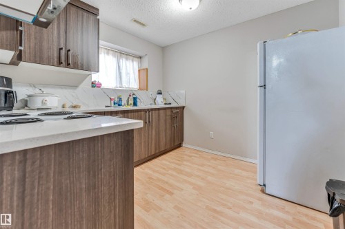 Kitchen featuring wood-finish cabinetry, light-toned countertops, a white tile backsplash, and light wood-finish flooring - 3519 22 Street Nw, Edmonton, AB 