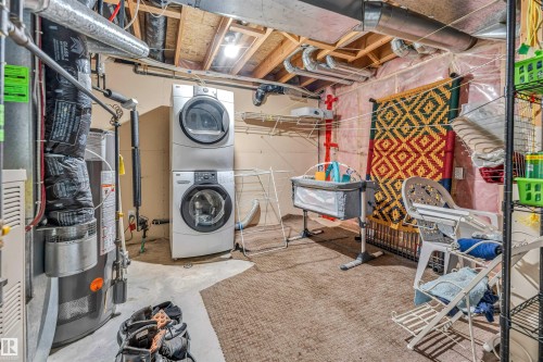 Dedicated utility area featuring a stacked washer and dryer, exposed ceiling joists with visible ductwork, and a water heater - 3519 22 Street Nw, Edmonton, AB 