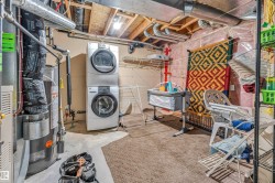 Dedicated utility area featuring a stacked washer and dryer, exposed ceiling joists with visible ductwork, and a water heater - 