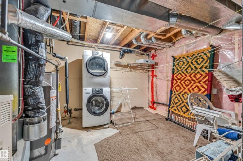 Dedicated utility area featuring a stacked washer and dryer unit, exposed ceiling joists, and visible ductwork - 3519 22 Street Nw, Edmonton, AB 