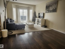 Spacious living area featuring bay windows, a glass-paneled balcony door, wood-finish flooring, and light-toned wall paint - 