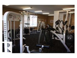 Fitness center featuring multiple exercise machines, textured dark carpeting, beige wall tones, and recessed lighting - 