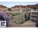 Concrete balcony with white metal railing overlooking a paved parking area and multi-story residential buildings with brown roofs - 425 4304 139 Avenue, Edmonton, AB 