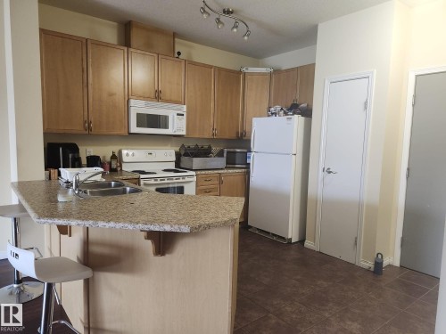 Kitchen featuring wood cabinetry, granite-finish countertops, and a double basin sink - 425 4304 139 Avenue, Edmonton, AB 