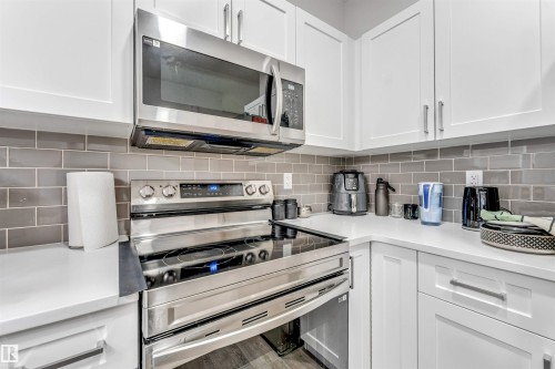 Corner kitchen featuring white upper and lower cabinetry, stainless steel range with electric cooktop, stainless steel over-the-range microwave, gray subway tile backsplash, and light-toned countertops - 45 2710 66 Street, Edmonton, AB 