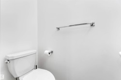 White wall finishes complemented by a contemporary white toilet and chrome fixtures, including a towel bar and toilet paper holder - 