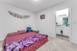 Carpeted bedroom with a bright white wall finish and a doorway revealing a bathroom with a white vanity and tiled flooring - 