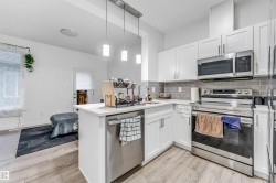 Modern kitchen featuring white shaker cabinetry, stainless steel appliances, light wood-finish flooring, a white countertop island with a built-in sink, and a gray subway tile backsplash - 