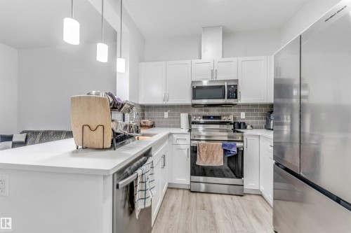 Modern kitchen featuring white shaker cabinetry, stainless steel appliances, a subway tile backsplash, and light wood-finish flooring - 45 2710 66 Street, Edmonton, AB 