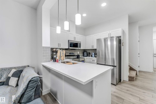 Modern kitchen featuring white cabinetry, stainless steel appliances, a subway tile backsplash, and light-toned wood-finish flooring - 45 2710 66 Street, Edmonton, AB 