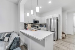 Modern kitchen featuring white cabinetry, stainless steel appliances, a subway tile backsplash, and light-toned wood-finish flooring - 