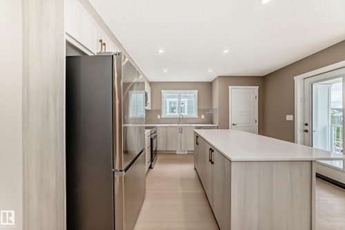 Modern kitchen featuring a large central island with a light-colored countertop, stainless steel appliances, light wood-finish cabinetry, recessed lighting, and a sliding glass door leading to a balcony - 1210 Stoneside Road, Sherwood Park, AB - Indoor Photo Showing Kitchen With Upgraded Kitchen