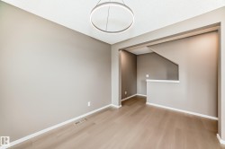 Open concept room featuring wood-finish flooring, neutral-toned walls, white trim, and a contemporary circular pendant light fixture - 