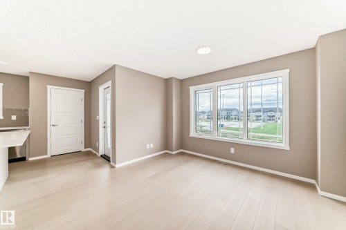 Open concept living space featuring light wood-finish flooring, a trio of large windows with grid accents, neutral wall paint, and white trim - 1210 Stoneside Road, Sherwood Park, AB - Indoor Photo Showing Other Room