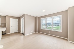 Open concept living space featuring light wood-finish flooring, a trio of large windows with grid accents, neutral wall paint, and white trim - 