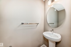 Pedestal sink with chrome faucet, circular mirror, and wall-mounted light fixture - 