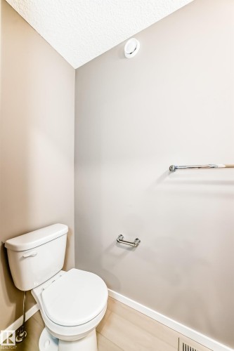 White toilet with chrome flush lever, light wood-finish flooring, and neutral wall paint - 1210 Stoneside Road, Sherwood Park, AB - Indoor Photo Showing Bathroom