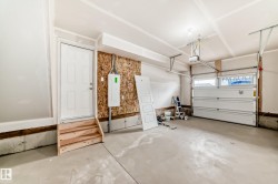 Spacious garage featuring a concrete floor, an overhead garage door with an automatic opener, exposed OSB wall sheathing, and a service entry door with wooden steps - 
