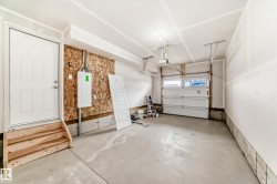 Spacious garage featuring a concrete floor, an overhead garage door, a pedestrian door with a three-step wood staircase, and an exposed wood panel wall with electrical panel - 