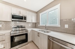 Contemporary kitchen featuring light wood-finish cabinetry, stainless steel appliances, white countertops, and a gray subway tile backsplash - 