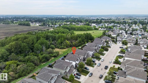 Aerial perspective showcasing a residential street with homes featuring light-toned exteriors and dark roofing - 64 South Creek Wynd, Stony Plain, AB 