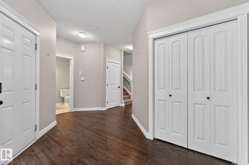 Hallway featuring wood-finish flooring, light-toned wall paint, white trim, and a white bi-fold closet door - 64 South Creek Wynd, Stony Plain, AB 