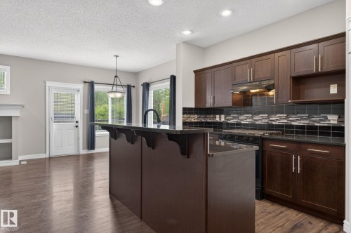 Kitchen featuring dark wood cabinetry, a black appliance suite, and a multi-textured black tile backsplash - 64 South Creek Wynd, Stony Plain, AB 