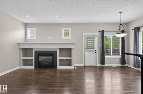 Spacious interior featuring dark wood-finish flooring, a built-in fireplace with black surround, integrated shelving, and recessed lighting - 64 South Creek Wynd, Stony Plain, AB 