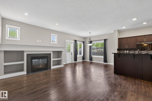 Living area featuring a fireplace with built-in shelving, wood-finish flooring, recessed lighting, and a kitchen island with dark wood cabinetry - 64 South Creek Wynd, Stony Plain, AB 