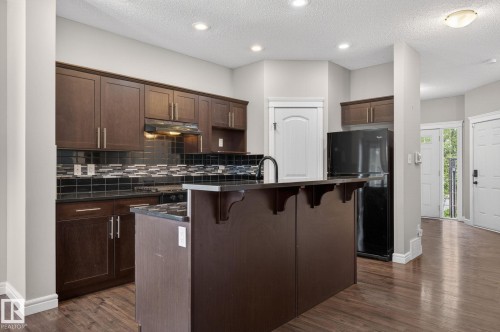 Kitchen featuring dark wood-finish cabinetry, black tile backsplash, and a central island with a dark countertop - 64 South Creek Wynd, Stony Plain, AB 