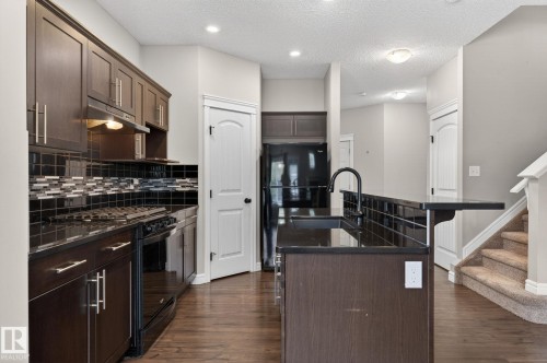 Kitchen featuring dark wood cabinetry, a black tile backsplash, and a central island with a sink and breakfast bar - 64 South Creek Wynd, Stony Plain, AB 