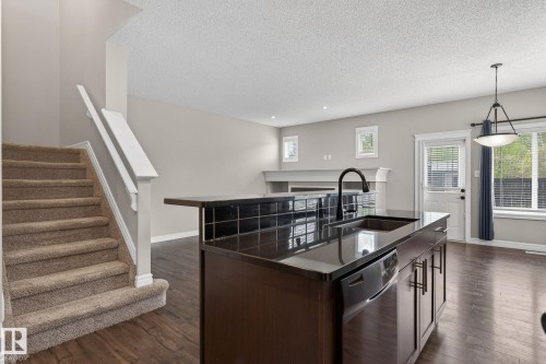 Kitchen island with dark cabinetry, integrated sink, and black countertop - 64 South Creek Wynd, Stony Plain, AB 