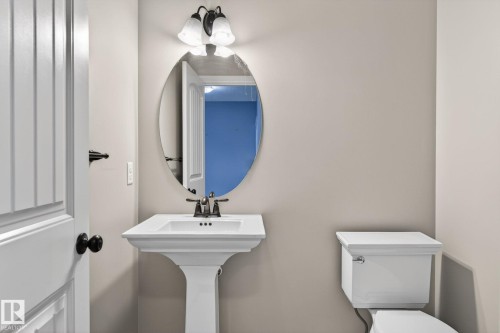 Bathroom featuring a white pedestal sink with a dark bronze faucet, an oval mirror, and a dark bronze vanity light fixture - 64 South Creek Wynd, Stony Plain, AB 