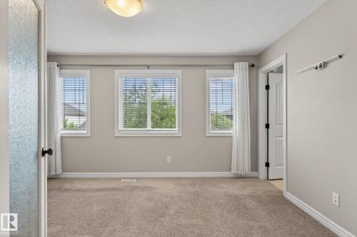 Carpeted room featuring three windows with horizontal blinds, light beige wall paint, white baseboards, and a semi-flush mount ceiling light - 64 South Creek Wynd, Stony Plain, AB 