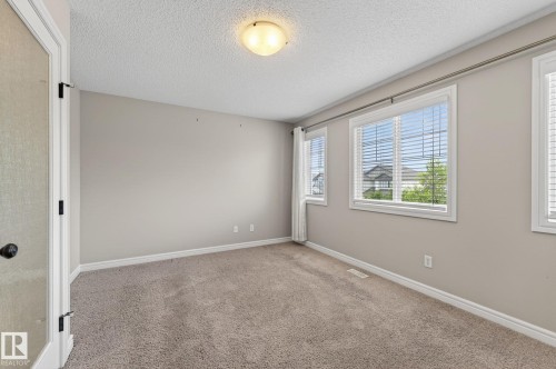 Carpeted room featuring multiple windows, a ceiling-mounted light fixture, neutral wall paint, white baseboards, and a door with frosted glass - 64 South Creek Wynd, Stony Plain, AB 