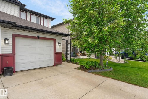Attached single-car garage with panel door, concrete driveway, and exterior lighting fixtures - 64 South Creek Wynd, Stony Plain, AB 