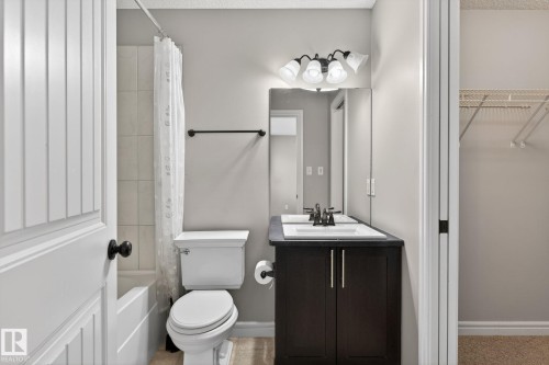 Bathroom featuring a dark wood-finish vanity with dual sinks, a large mirror, and an overhead four-light fixture - 64 South Creek Wynd, Stony Plain, AB 