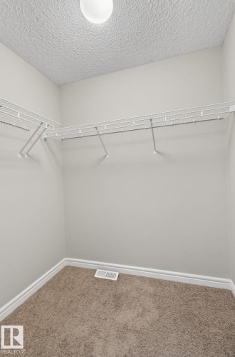 Walk-in closet with wire shelving system, recessed ceiling light, textured ceiling, light gray walls, and brown carpet flooring - 64 South Creek Wynd, Stony Plain, AB 