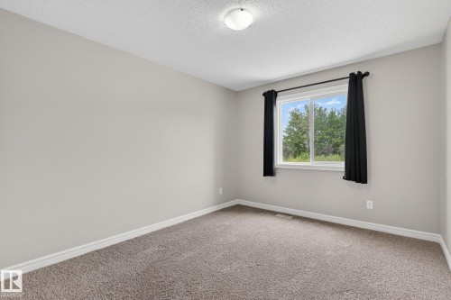 Carpeted room featuring light gray walls, white baseboards, and a window with a green tree backdrop - 64 South Creek Wynd, Stony Plain, AB 