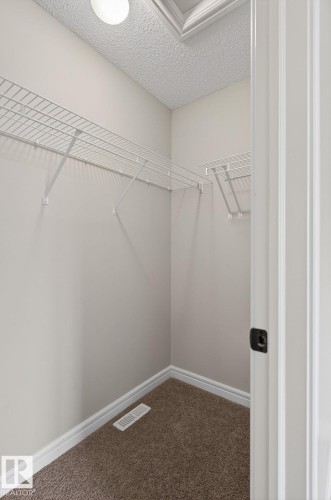 Walk-in closet featuring wire shelving, neutral carpeting, a white baseboard trim, and a ceiling light fixture - 64 South Creek Wynd, Stony Plain, AB 