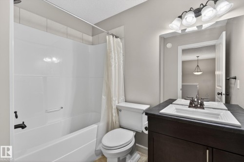 Full bathroom featuring a white tub/shower combination with black fixtures, a white toilet, and a dark wood-finish vanity with a white rectangular sink and dark countertop - 64 South Creek Wynd, Stony Plain, AB 